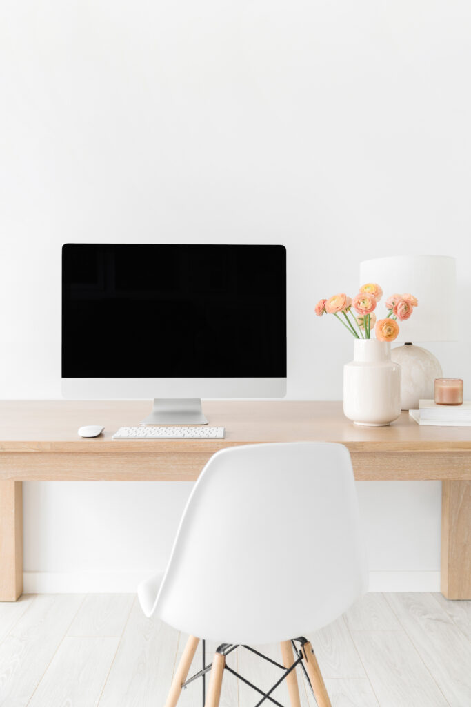 desktop computer on desk with flowers and white chair